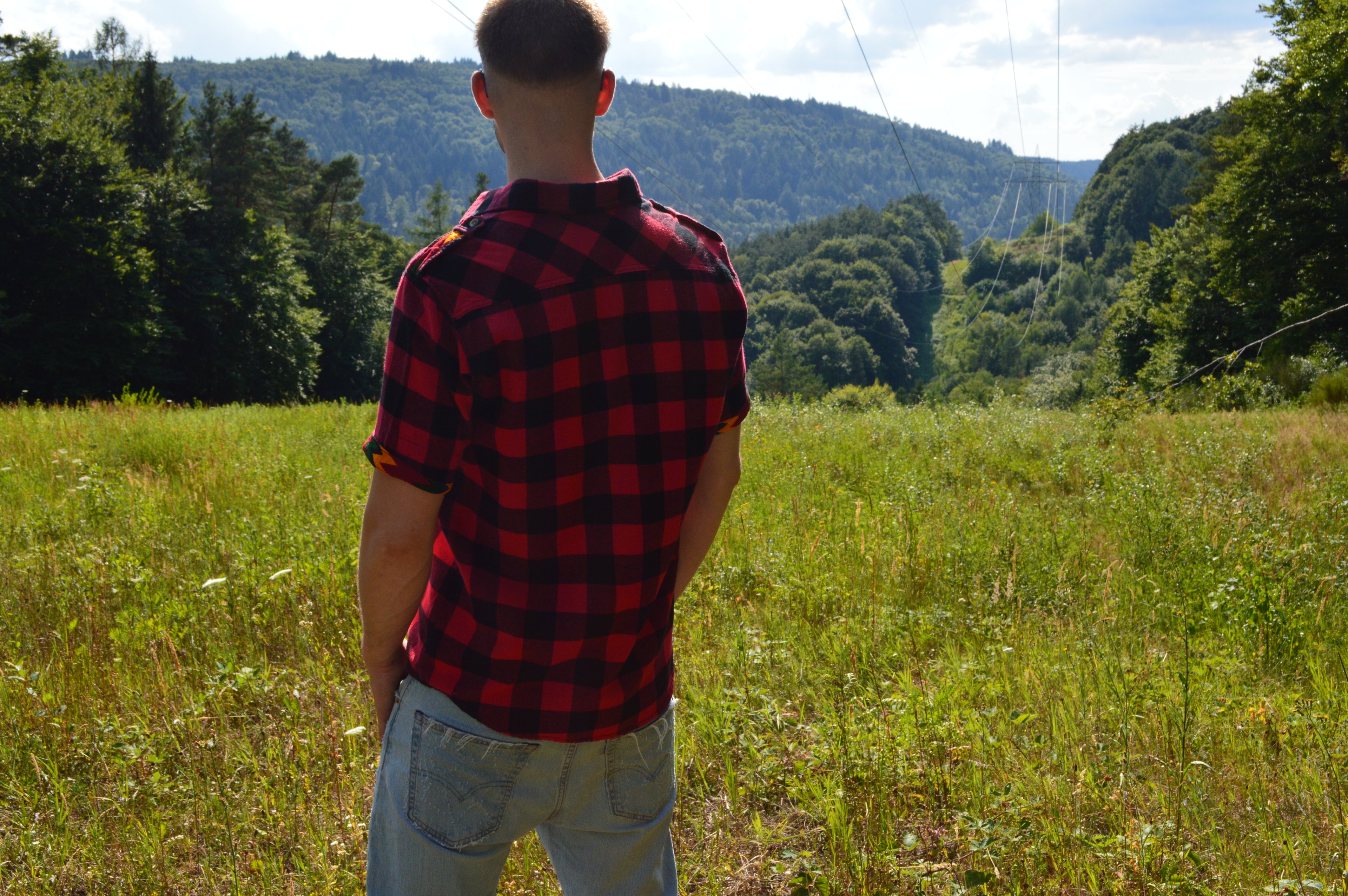 Model Trägt rotschwarz karriertes Afari Flanell Kurzarm Hemd und blickt auf das Tal mit dem rücken zur Kamera