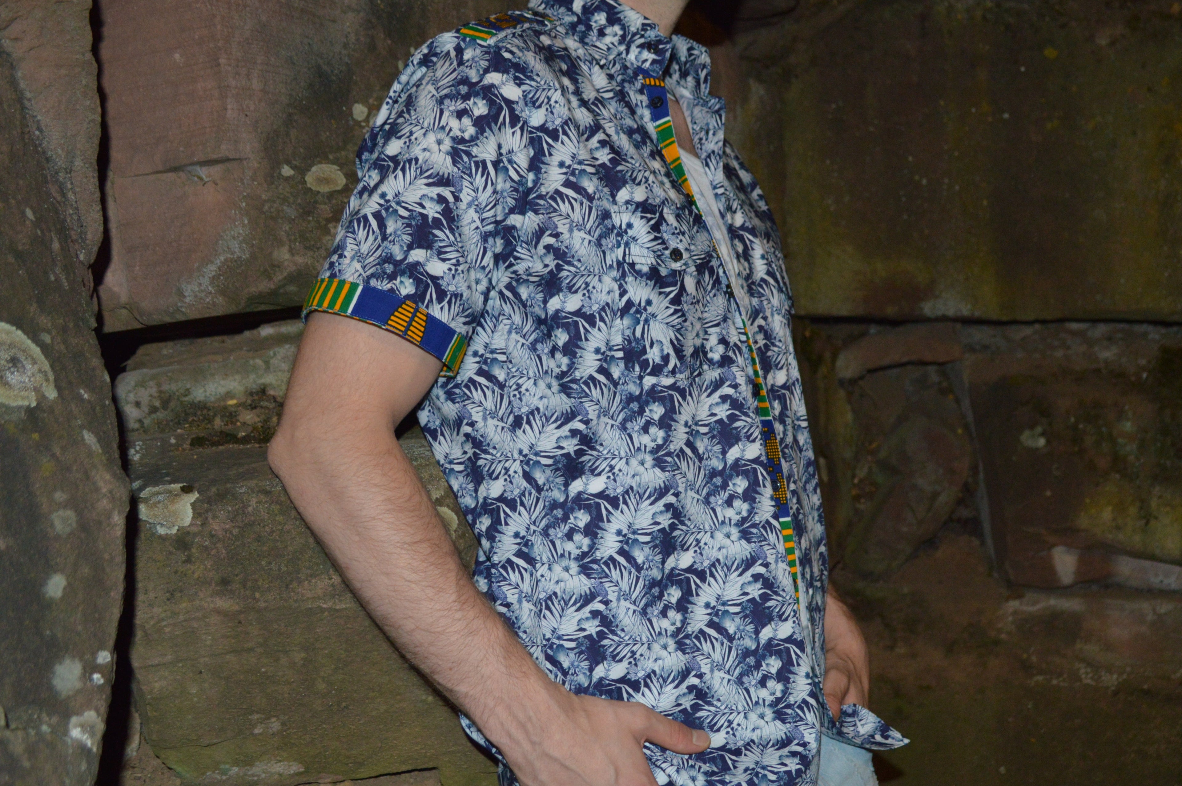 Model possiert lässig an Steinwand mit einem Kurzarm Hemd.