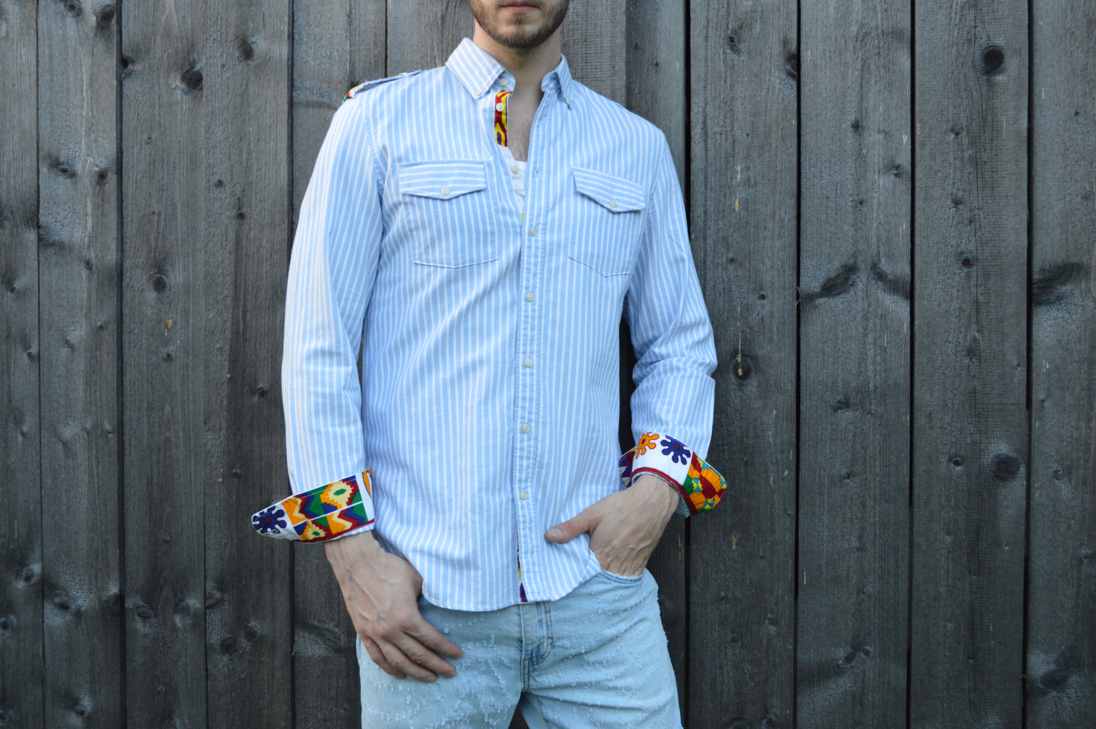 Model possiert  frontal zur Kamera gewendet in einem blau weis gestreiften Langarm Hemd.