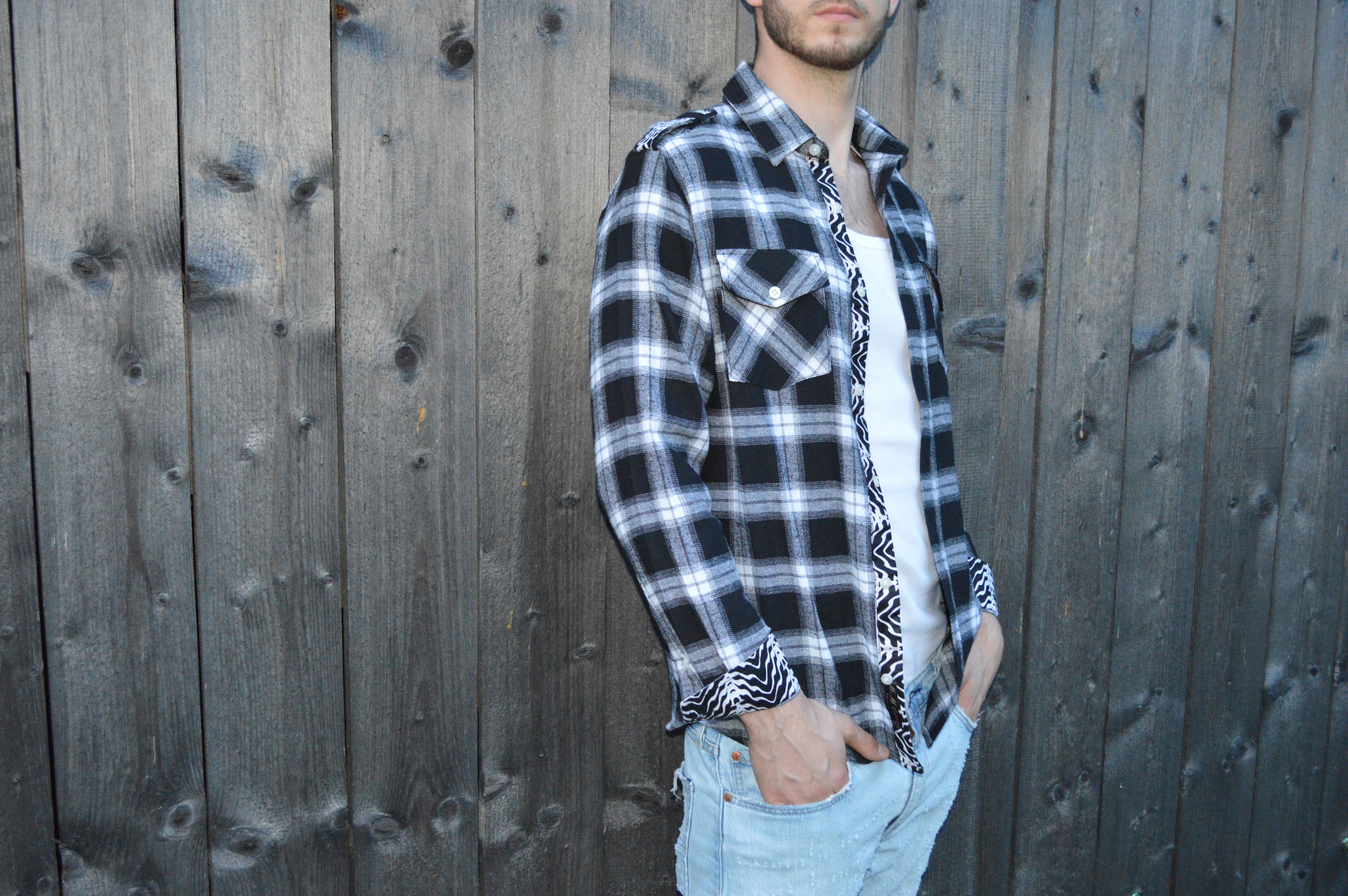 Model possiert schräk zur Kamera gewendet in einem schwarzweis karrierten Langarm Hemd.