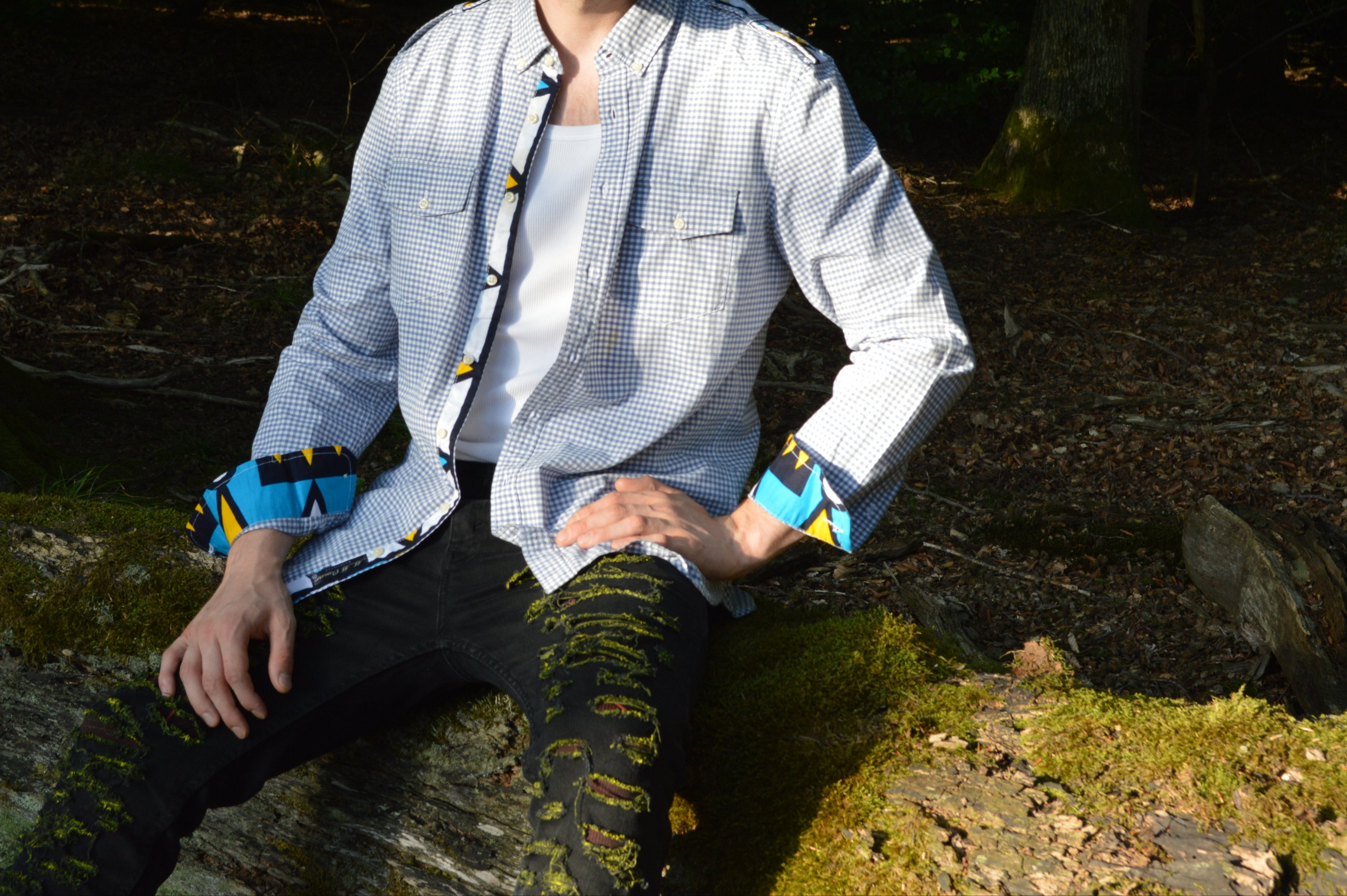 Model präsentiert Langarm Afari Hemd, sitzend auf einem Baumstamm im Wald.